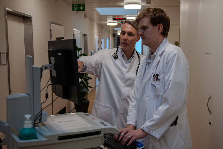 Leitender Arzt mit Assistenzarzt bei der Besprechung vor der Visite eines Parkinson-Patienten 